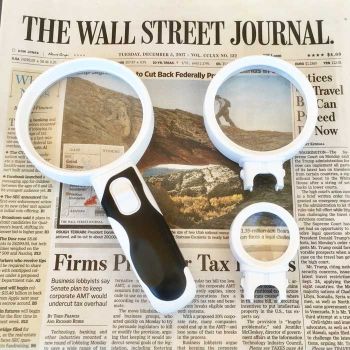 white and grey led magnifier with 3 interchangeable lenses 2x 4x and 10x lenses lying on wall street journal