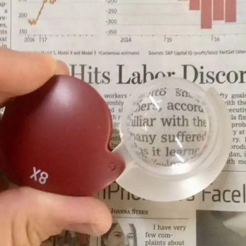 red hard cased folding 8x magnifier magnifying text in a business section of newspaper